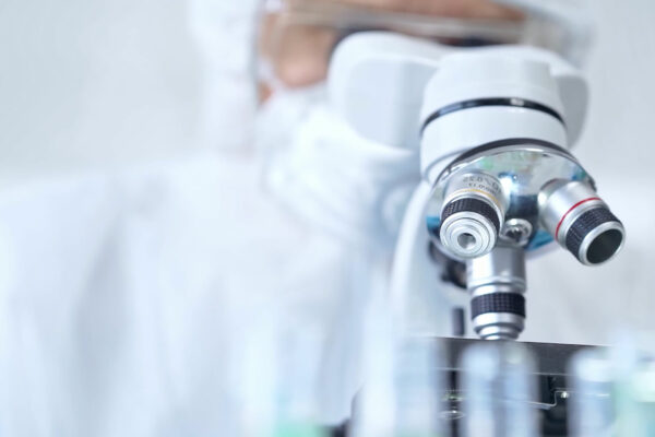 Professional scientist in protective gear is using microscope in a laboratory setting, close-up. Science and medicine concepts.